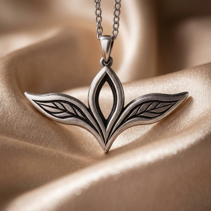 Close-up of the Elven Leaf Necklace on champagne fabric, showing the open center leaf and engraved veins in the two side leaves.