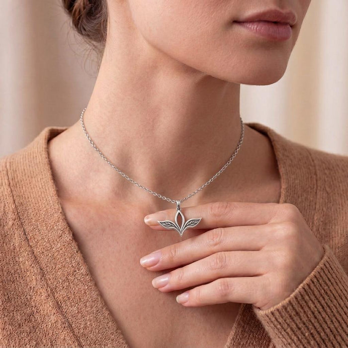 Model wearing the Elven Leaf Necklace with a tan knit top while holding the three-leaf pendant near the collarbone.