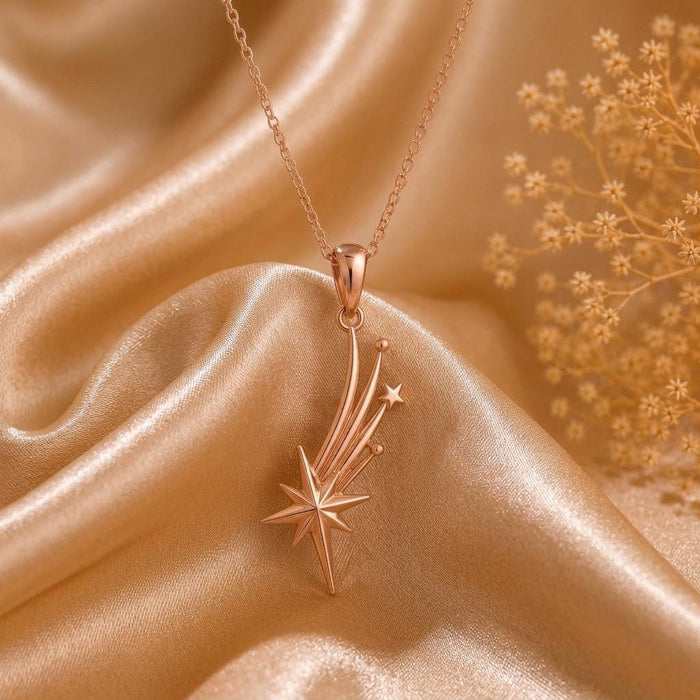 Rose Gold Plated Falling Star Pendant Necklace with curved star trails on champagne satin beside dried flowers