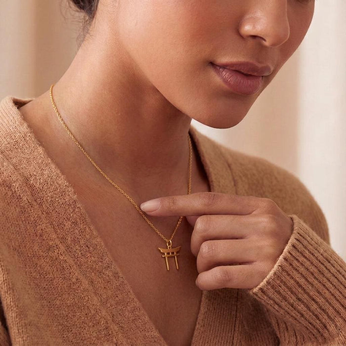 Gold Plated Silver Torii Gate Necklace held against a tan knit cardigan
