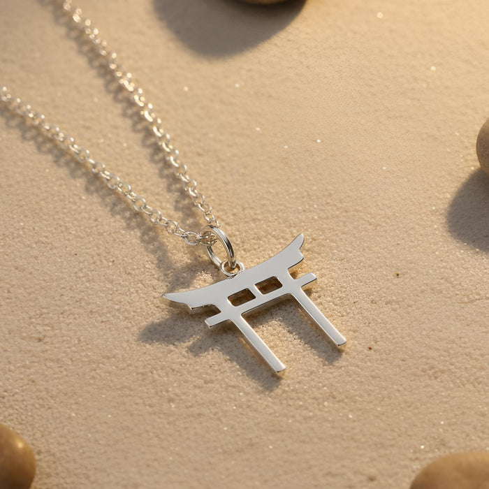 Silver Torii Gate Necklace on sand showing the curved crossbeam and rectangular openings