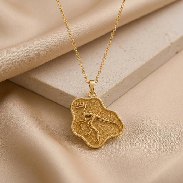 Gold Plated Silver Troodon fossil pendant displayed on beige stone and draped satin