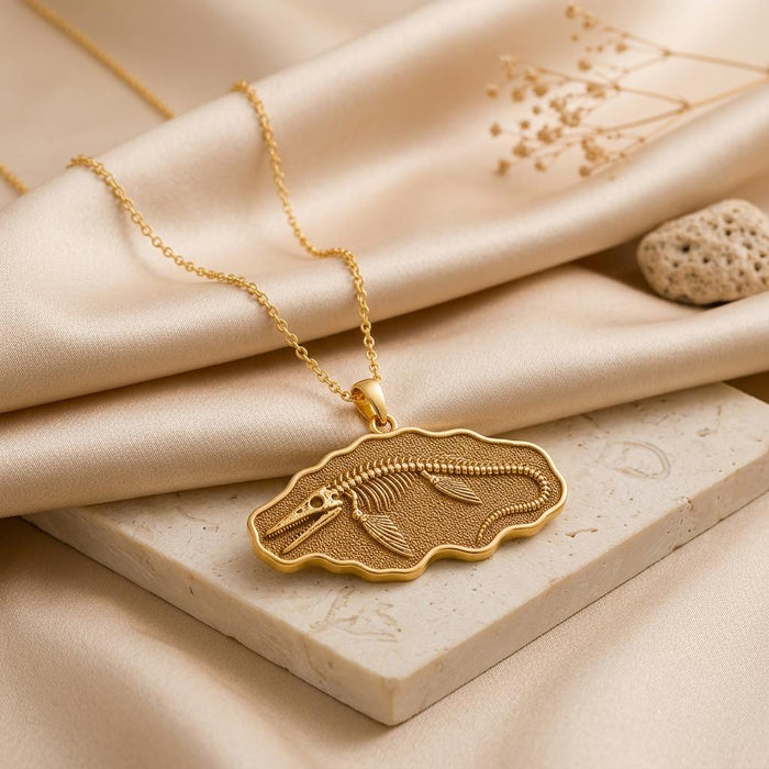 Gold Plated Silver Tylosaurus fossil pendant necklace displayed on a stone block with satin and dried botanicals