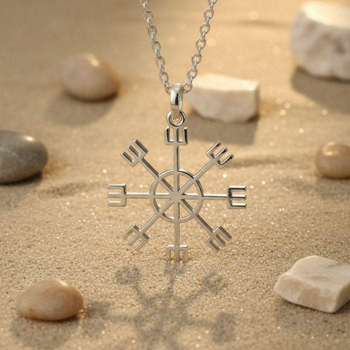 Silver Vegvisir Sun Compass Necklace hanging above sand with smooth stones