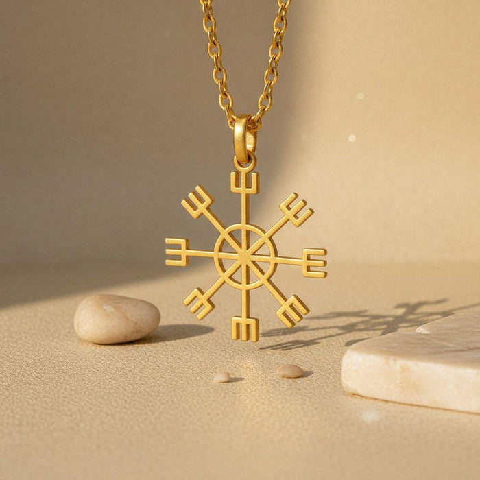 Gold Plated Silver Vegvisir Sun Compass pendant hanging above a sand-toned surface with stones