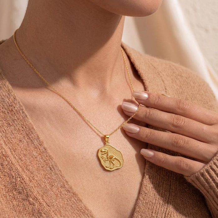 Gold-finish Velociraptor Fossil Pendant worn at the neckline with a neutral knit top