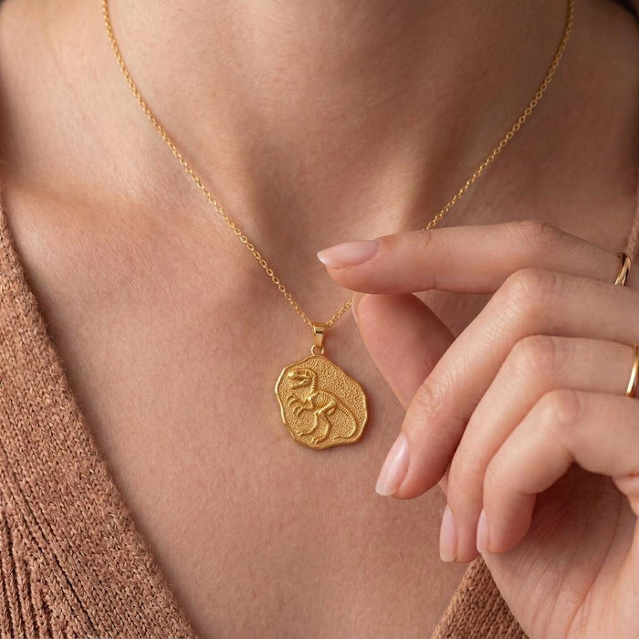 Close neckline view of a Gold Plated Silver Velociraptor Fossil Pendant held by hand