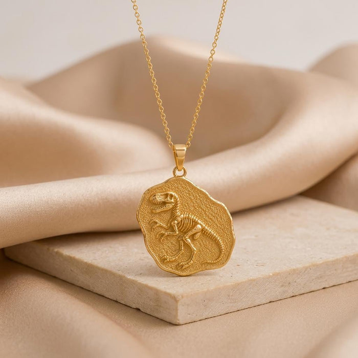Gold-finish Velociraptor Fossil Pendant on a pale stone slab with champagne satin