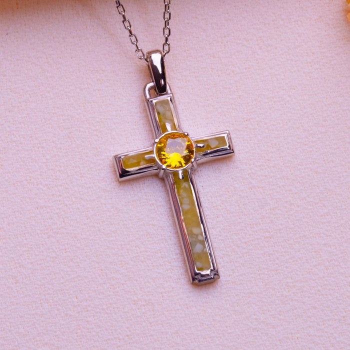 Close-up of the Vertical Framed Birthstone Cross Necklace with framed inset panels and a round yellow center stone on pale fabric