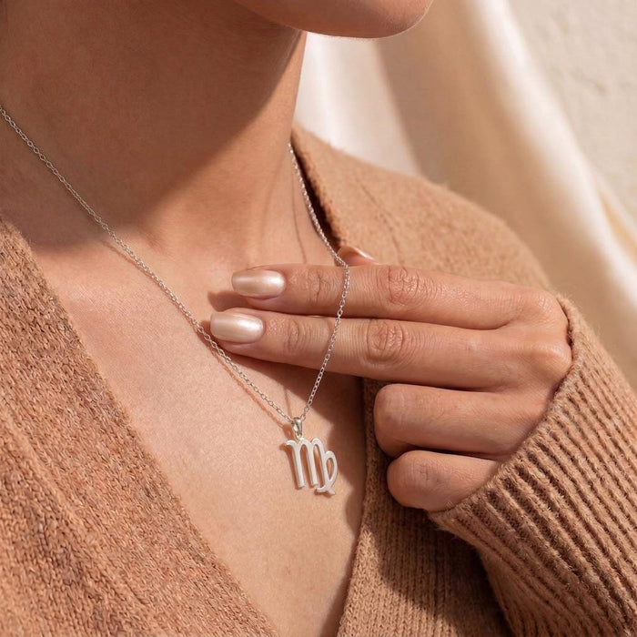 Virgo glyph necklace worn at the neckline with a hand near the pendant