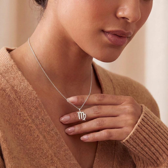 Virgo symbol necklace worn with a neutral knit top and hand detail