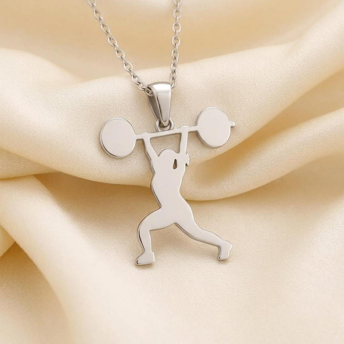 Overhead barbell athlete pendant necklace displayed on cream fabric