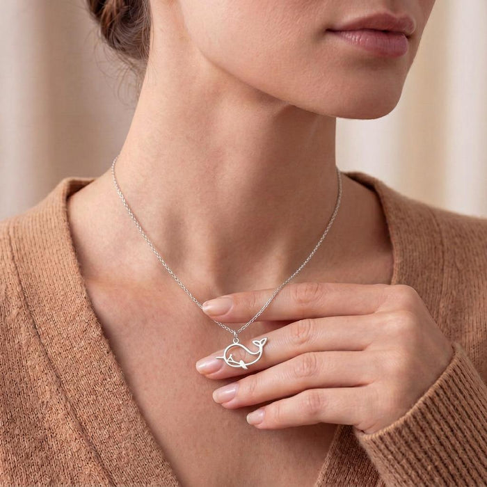 Model wearing a silver whale outline necklace while holding the pendant at the neckline