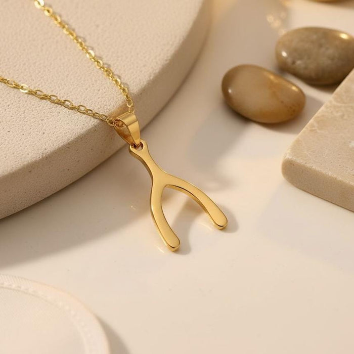 Gold Plated Silver Wishbone Necklace close-up on a cream surface beside smooth stones